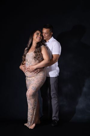 Intimate couple's maternity shoot with beaded gown against dark background.