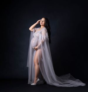 Dramatic maternity photos featuring sheer white flowing cape against dark background.