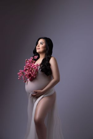 Artistic maternity portraits with pink flowers and flowing fabric.