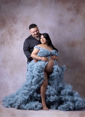 Maternity photography featuring dusty blue tulle dress against textured brown backdrop.