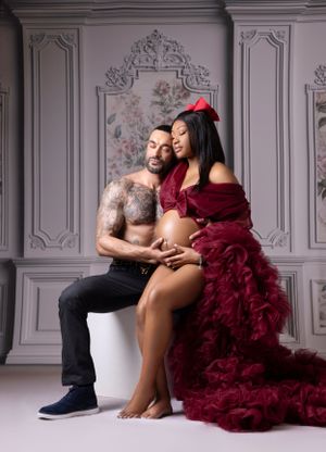 An intimate maternity photo with a dramatic burgundy robe against an ornate grey wall backdrop.