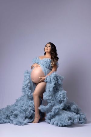 Maternity photos featuring flowing blue tulle fabric in studio setting.