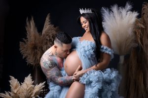 Ethereal maternity photoshoot with flowing blue tulle dress and pampas grass decorations in dreamy lighting.