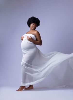 Artistic maternity portrait with flowing white fabric against light grey background.