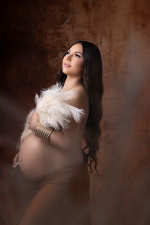Artistic maternity portraits with white feather accents against textured brown background.