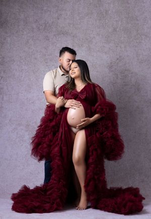 Maternity photography session featuring a burgundy tulle gown against a grey backdrop.