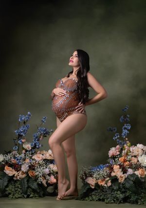 Artistic maternity photo shoot with floral arrangements and blue delphinium flowers against a dark background.
