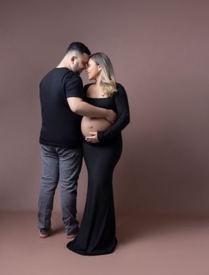 Intimate maternity photography session with couple wearing black outfits against mauve background.