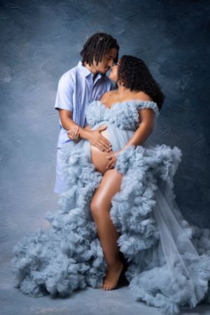 Maternity photos with flowing blue tulle dress in studio setting.