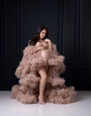 Luxurious maternity photos featuring billowing dusty rose tulle against dark walls.
