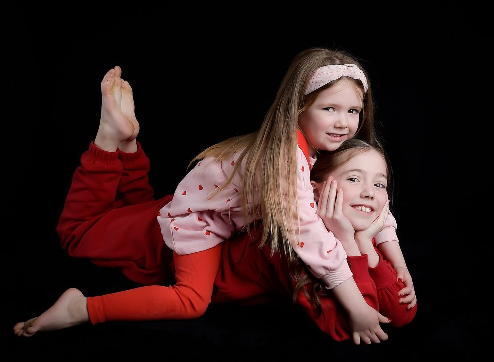 Dark fine art sisters portrait by Nicola in Woodside, moody studio lighting capturing a timeless, emotional sibling connection