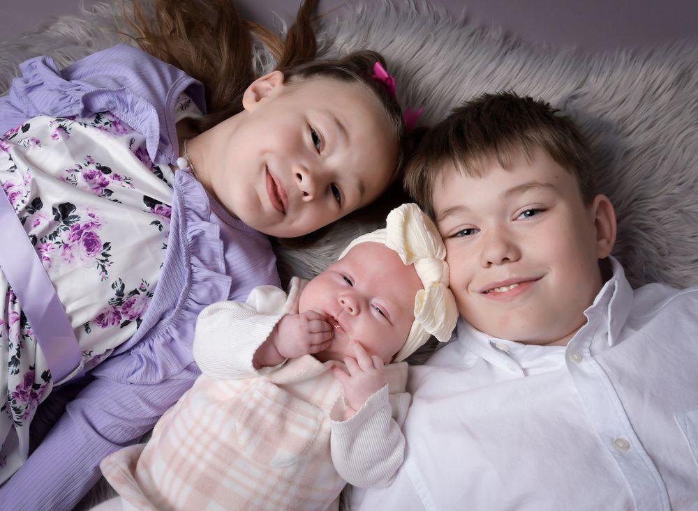 A big brother and sister introducing their new baby sister. Fluffy grey rug to create that cosy feel.