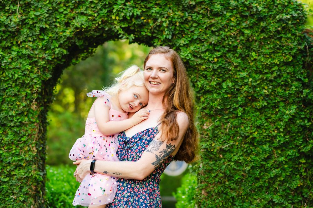 Two people share a happy moment together in a garden with a lush green hedge archway framing the scene.