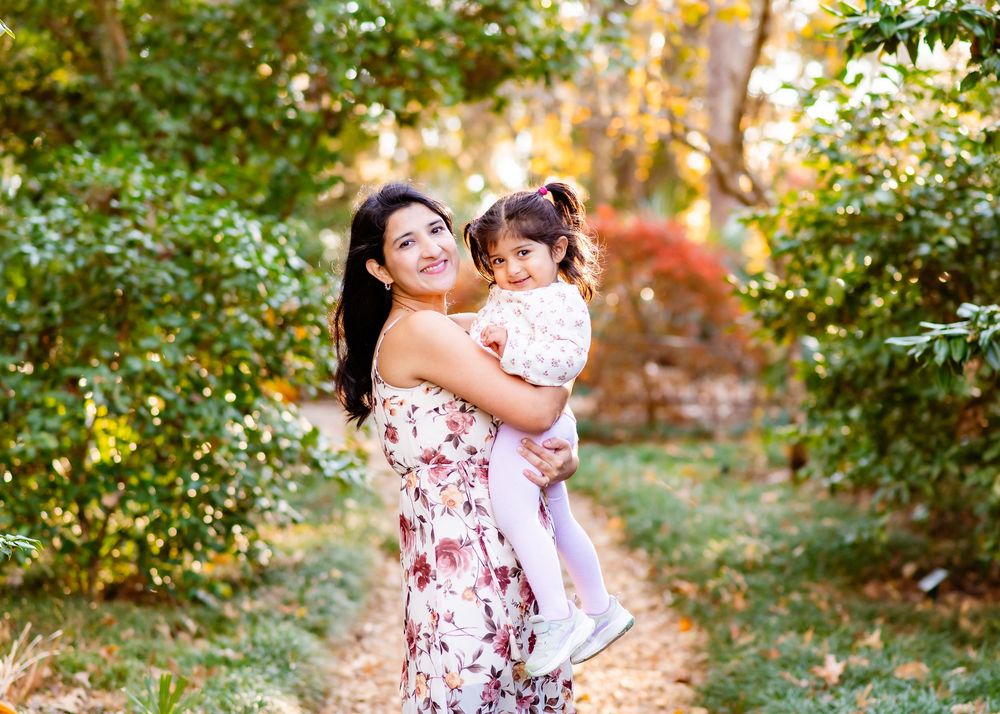 Two people in floral dresses embrace while standing in a sunlit garden during golden hour.