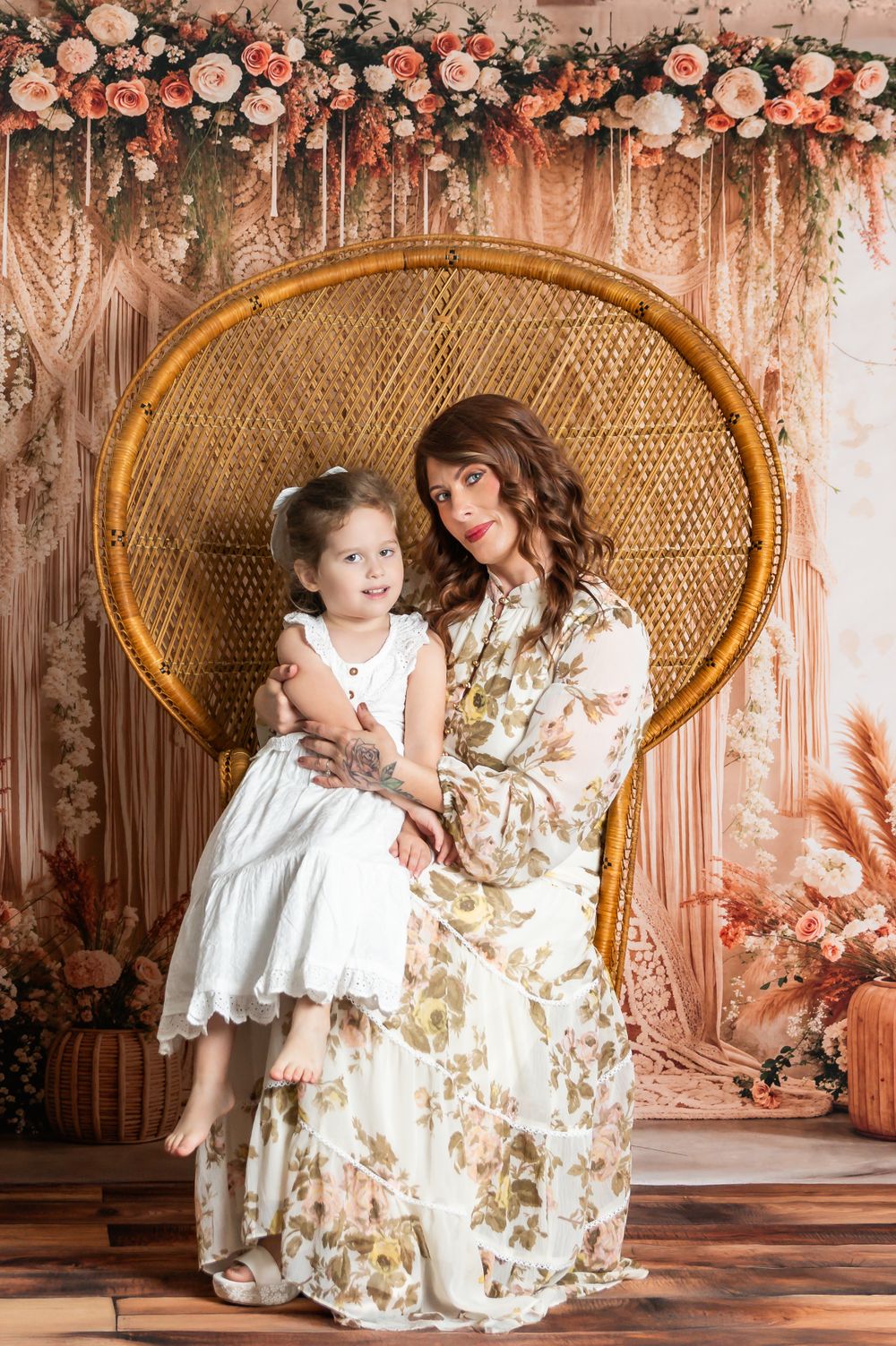 Beautiful floral backdrop with peacock chair and figures in matching white and floral dresses for elegant portrait session.