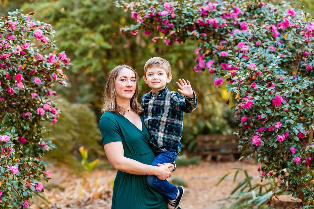 A family shares tender moments among blooming pink flowers in a lush garden setting during a photo session.