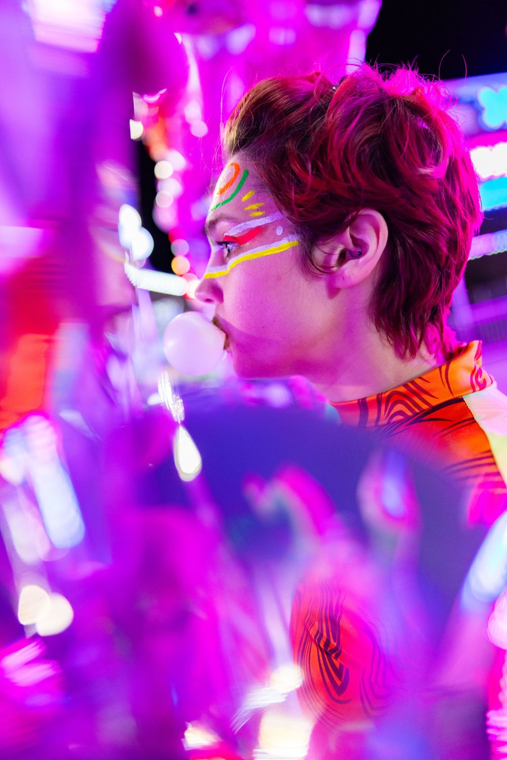 Artistic profile shot with colorful face paint illuminated by purple and pink neon lights.