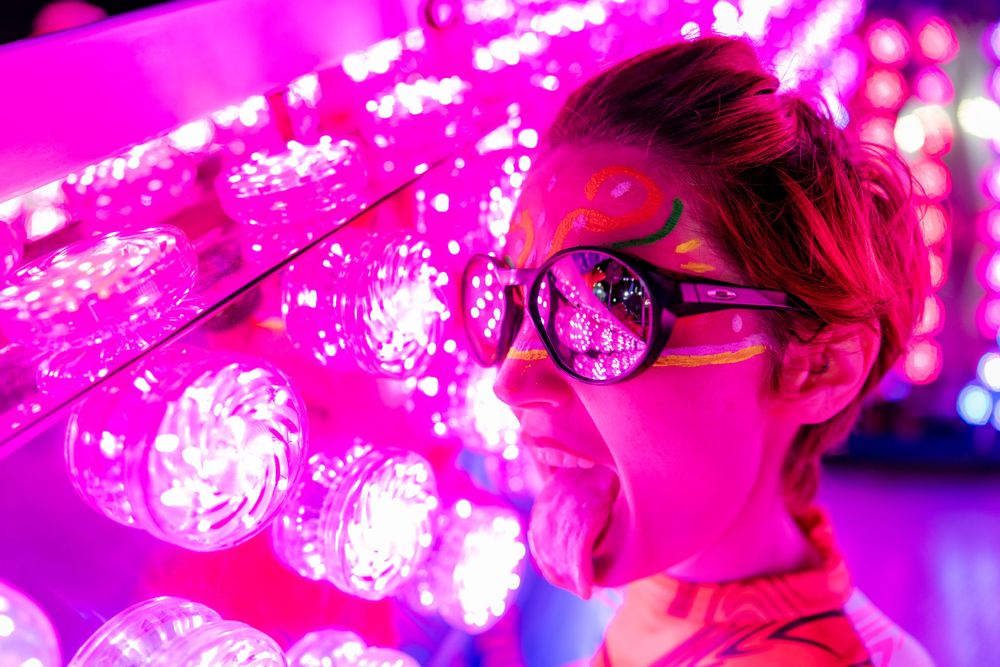 Pink neon lights illuminate figure wearing glasses in dark environment.