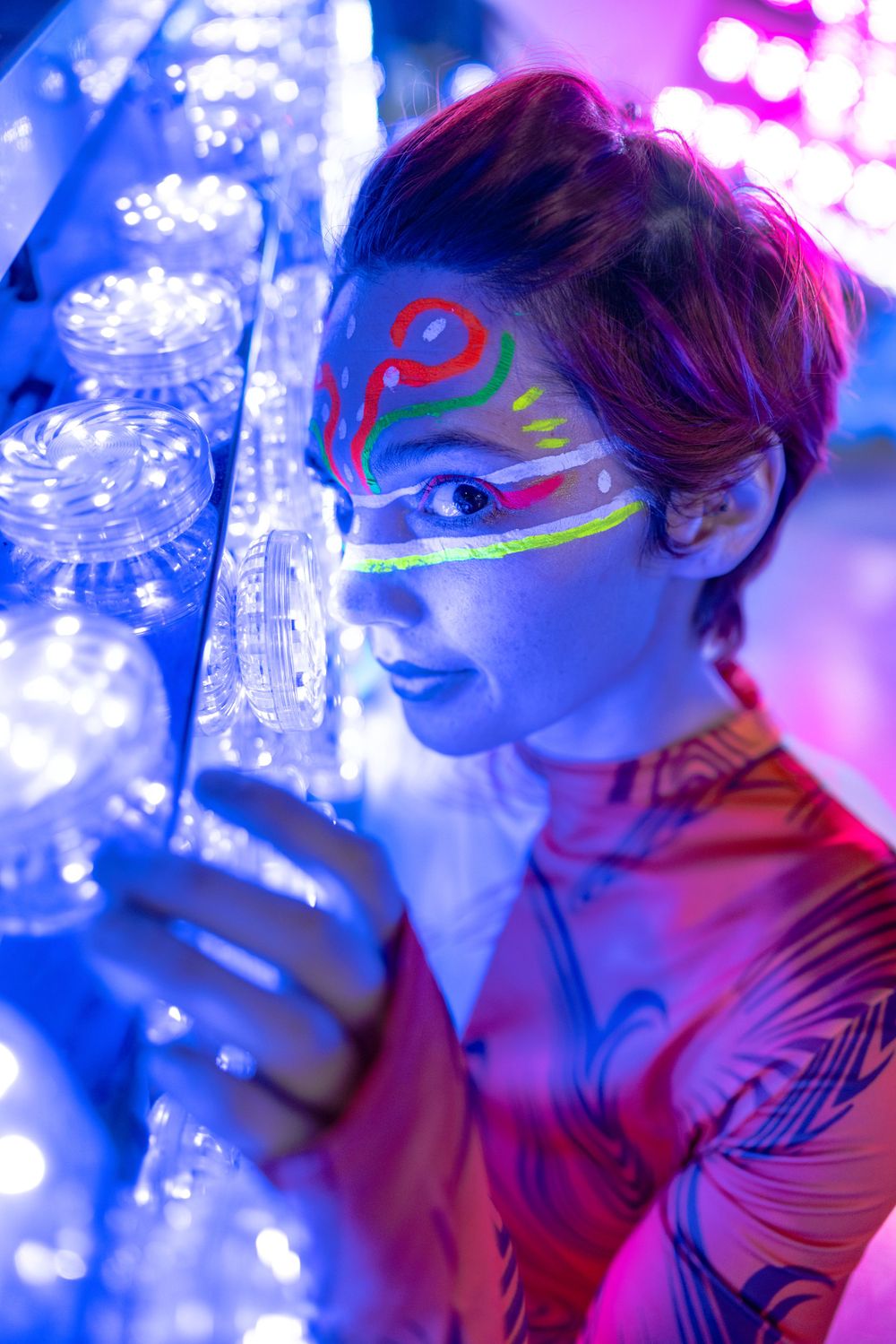 Creative portrait with neon face paint and blue lighting effects.
