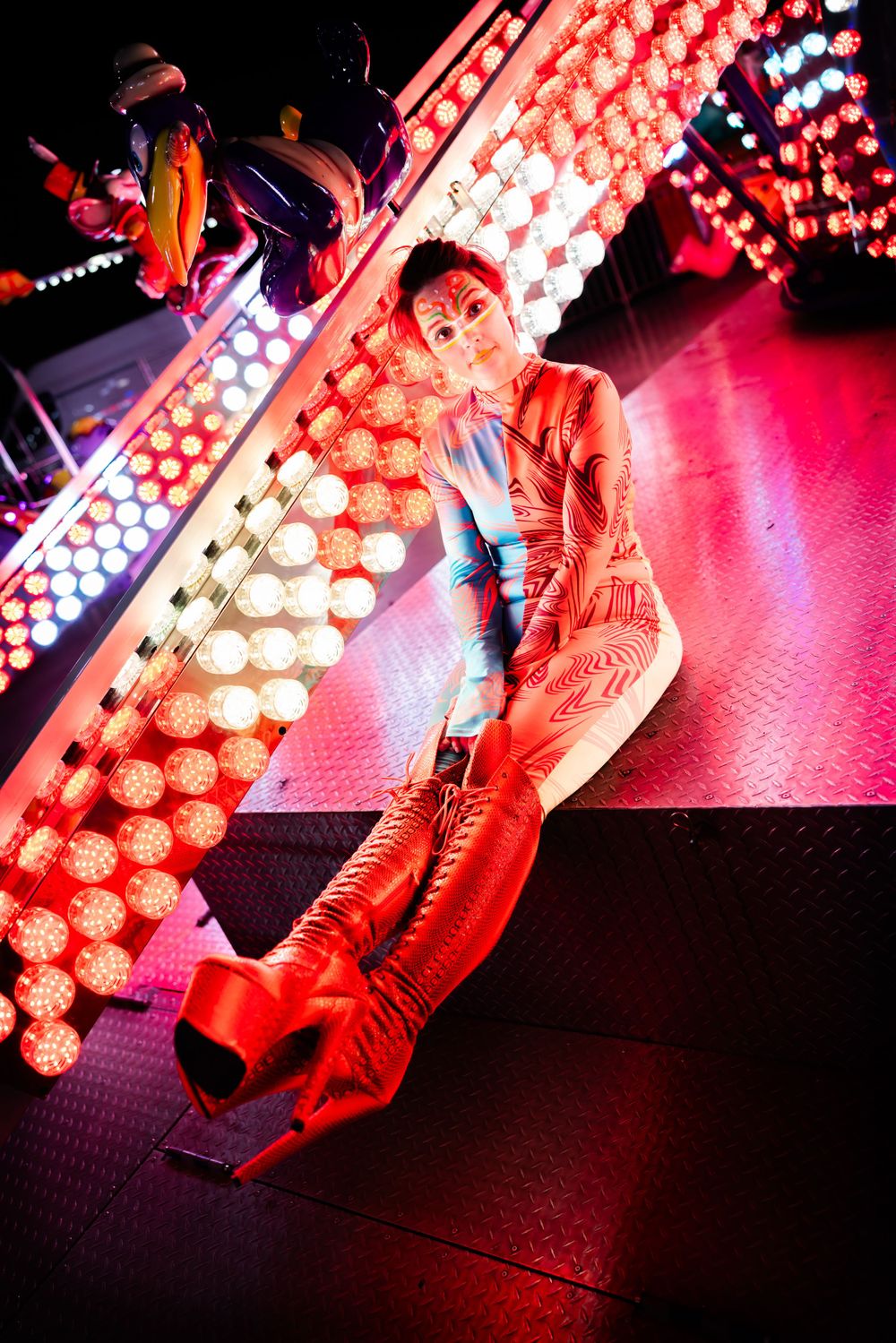 Dramatic red-lit carnival scene with performer in vibrant costume against bright lights.