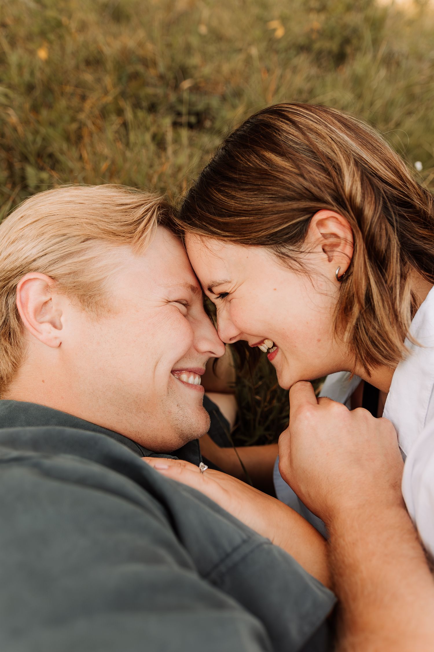 Couple snuggles in grass with faces pressed together