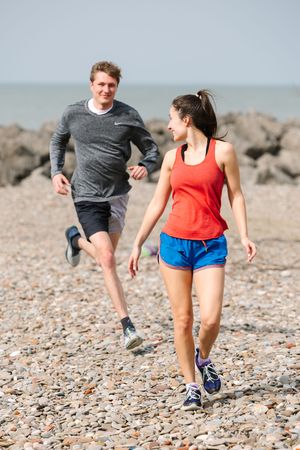 Two runners on pebble beach workout wearing athletic clothes exercise along rocky shoreline.