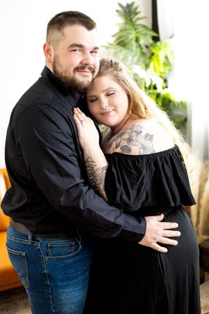 Intimate embrace captured in studio with orange couch and greenery in background.