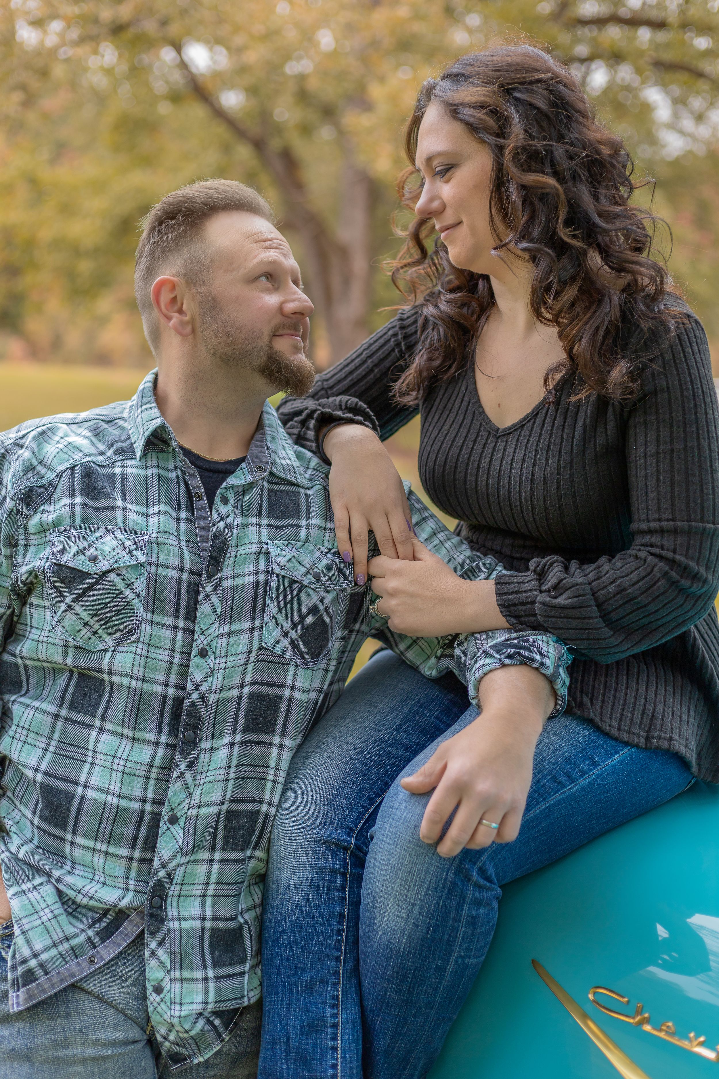 Couple sharing a playful moment while sitting on a turquoise surface during autumn.
