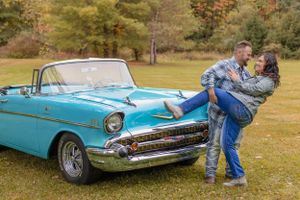 Couple embracing by a classic turquoise Chevrolet convertible in a fall setting.