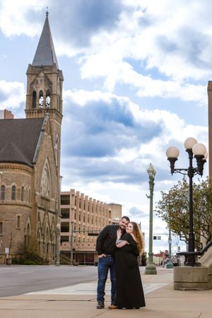 Romantic couple standing by historic church and street lamps in downtown setting.
