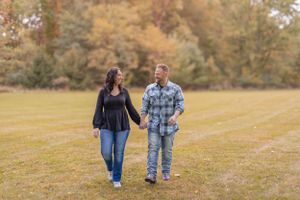 A couple walks hand in hand across a sunlit autumn field.
