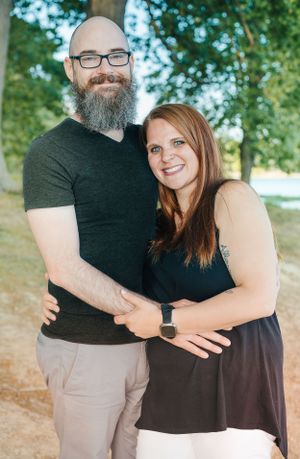 Couple wearing black tops posing together outdoors under trees.