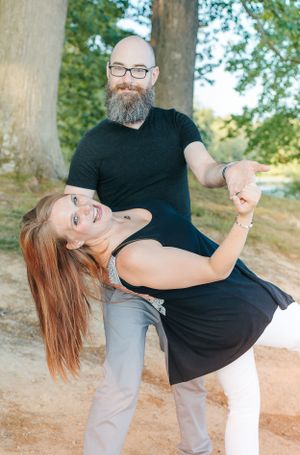 Playful couple in black attire dancing and dipping in an outdoor setting.