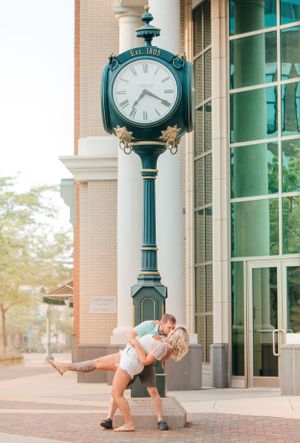 Couple dancing under decorative green clock post in downtown area.