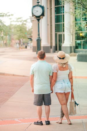 Couple in casual summer outfits walking together on a sidewalk with a decorative clock post.