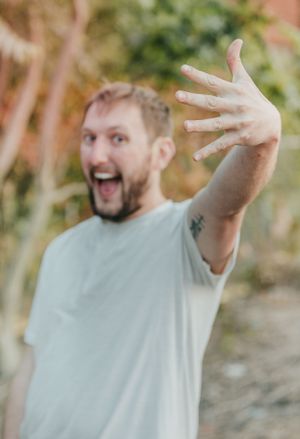 Person excitedly displaying engagement ring with animated expression.