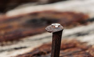 Diamond engagement ring balanced on rusty nail head in artistic macro shot.