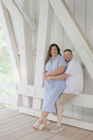A couple poses together inside a white covered bridge structure.