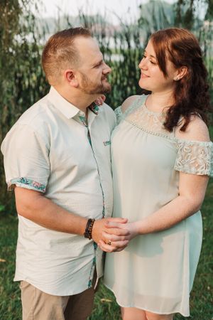 A couple in light-colored outfits share an intimate moment in a garden setting.