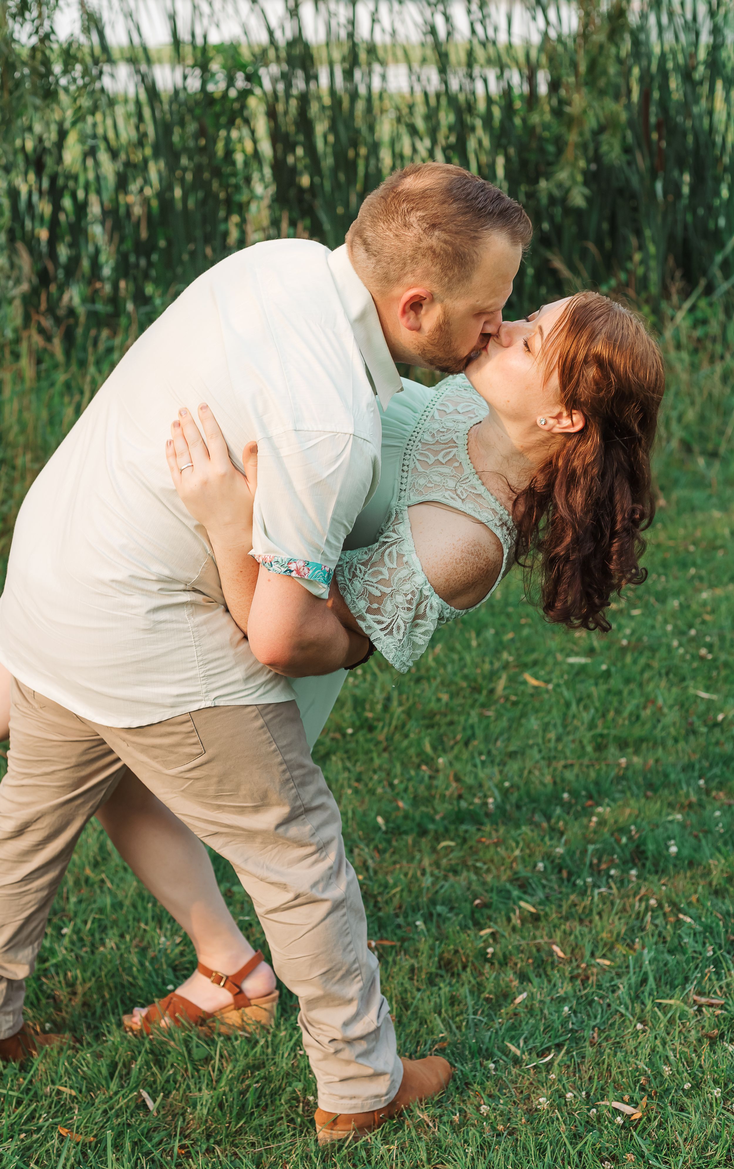 Romantic couple performs a dramatic dance dip pose on green grass.