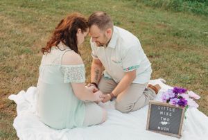 A couple sits on a picnic blanket with a small sign display outdoors.