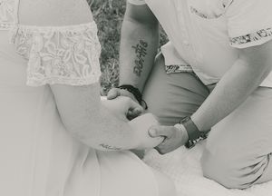 Black and white close-up of hands with visible tattoos clasped together.