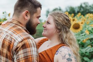 A romantic moment shared between a couple in a blooming sunflower field, wearing autumn-toned clothing.