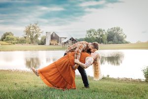 A romantic dip pose captured against a rustic farmland backdrop with a barn and pond.