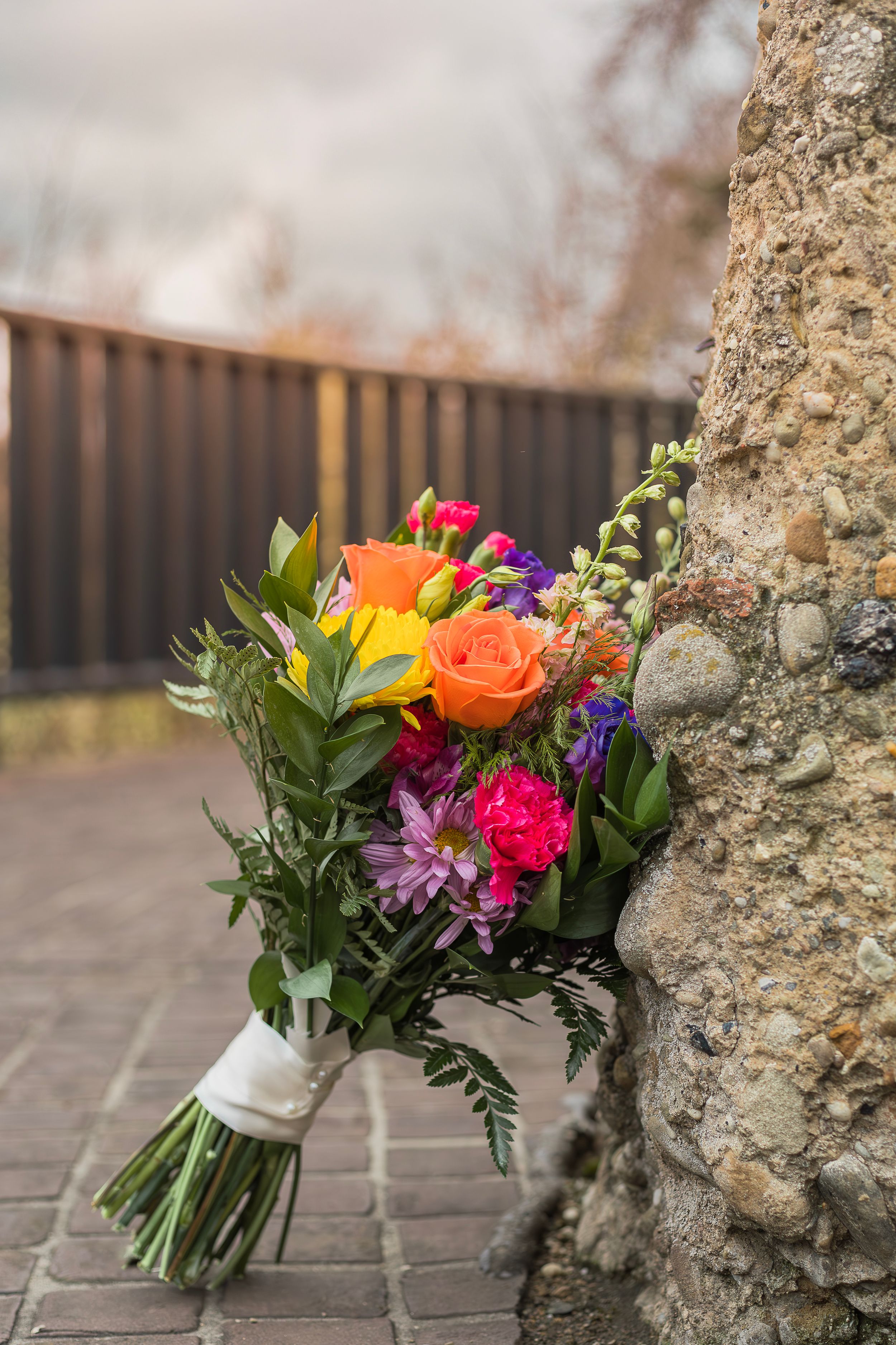 Colorful wedding bouquet with roses and mixed flowers leaning against a stone wall.