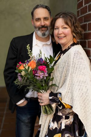 A couple poses with a colorful bouquet in formal attire.