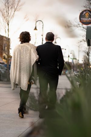 A couple walking together on a city sidewalk at dusk.
