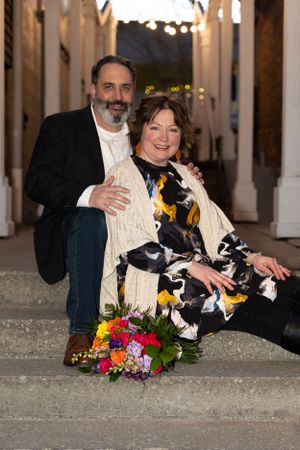 A couple sits on steps with a colorful bouquet at dusk.