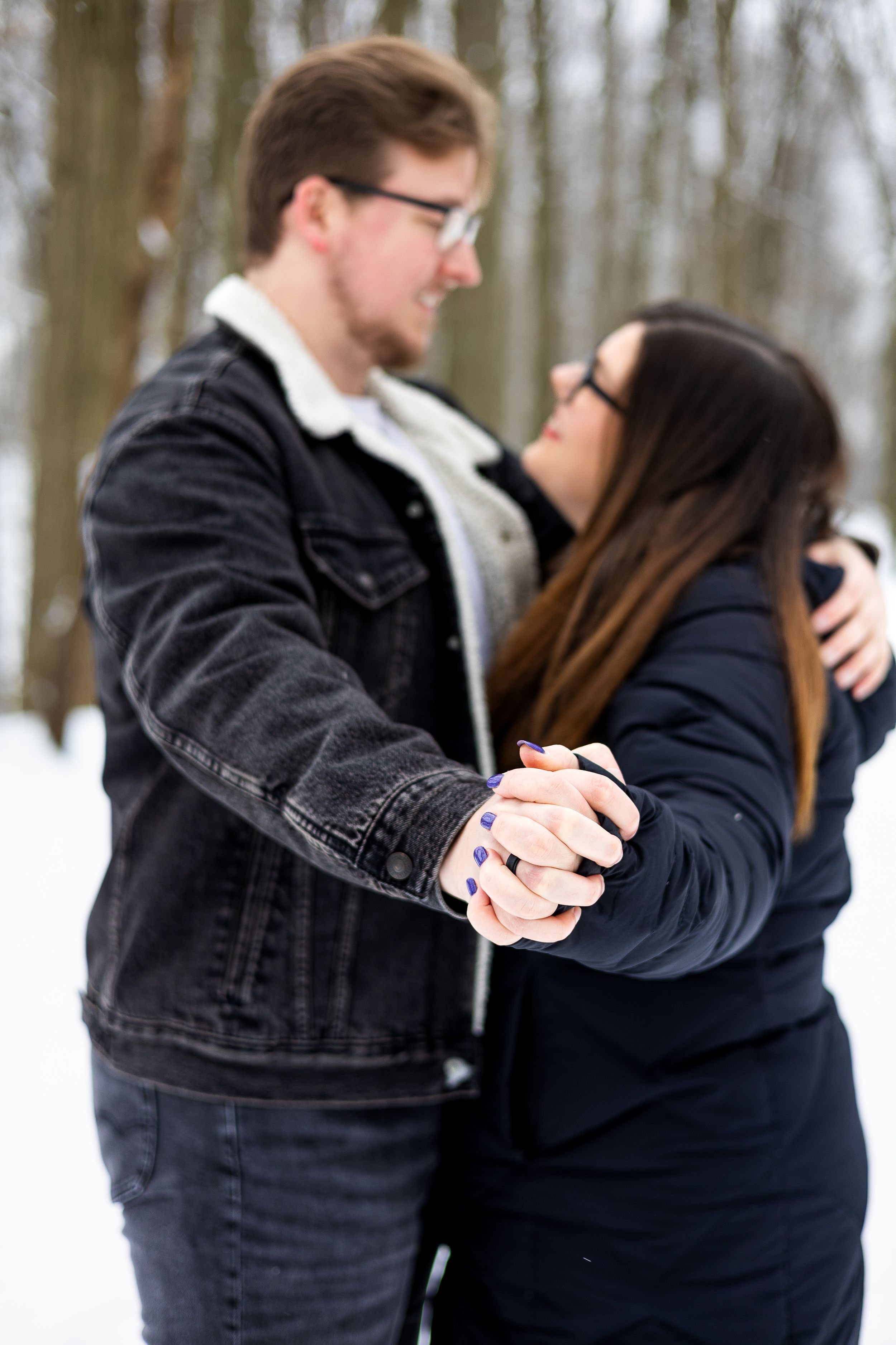 Couple wearing matching navy outfits embracing in a snowy forest during winter photoshoot.