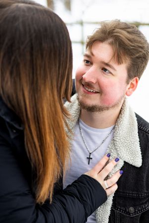 Close up of a romantic couple sharing an intimate moment outdoors, with one wearing a black jacket and cross necklace.